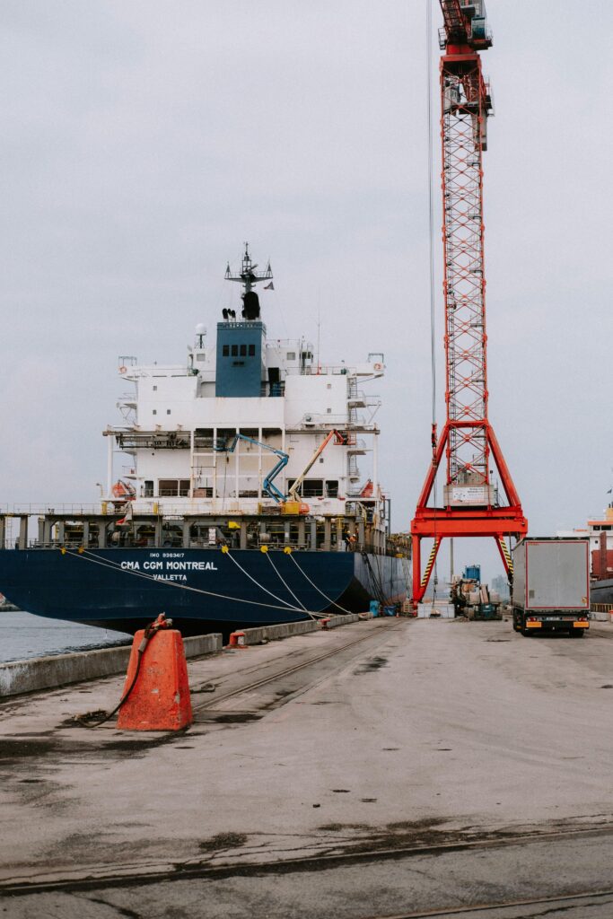 Container ship at a bustling port with cranes and trucks in view.
