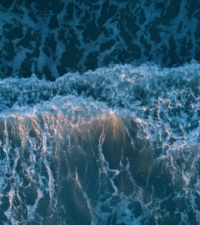 Breathtaking aerial view of crashing ocean waves at sunset, showcasing nature's beauty.